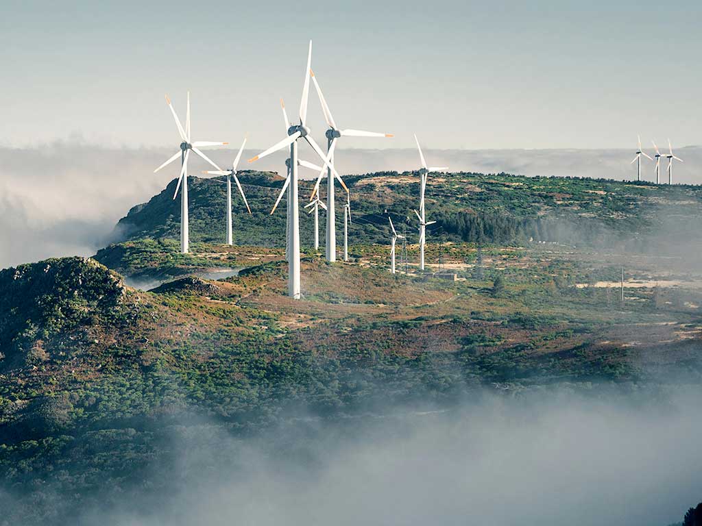 Mehrere Windräder auf einem Berg über einem Hochnebel